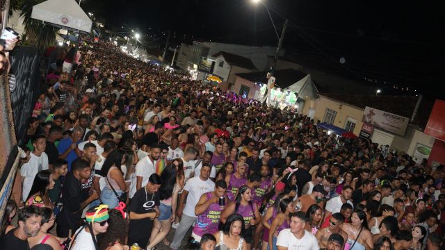 Multidão de foliões ocupa as ruas de Correntina durante o Carnaval à noite, com grande concentração de pessoas acompanhando a festa em espaço público iluminado.