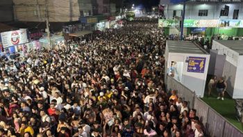 Multidão ocupa avenida durante o Carnaval de Correntina à noite, com grande concentração de foliões em frente a comércios e estruturas de camarote, sob iluminação pública e clima festivo.