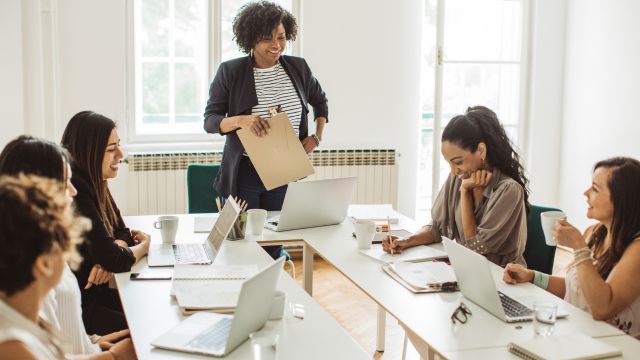 Grupo de mulheres reunidas em ambiente de trabalho, participando de reunião com uso de notebooks e anotações, representando atividade de empreendedorismo e colaboração profissional.