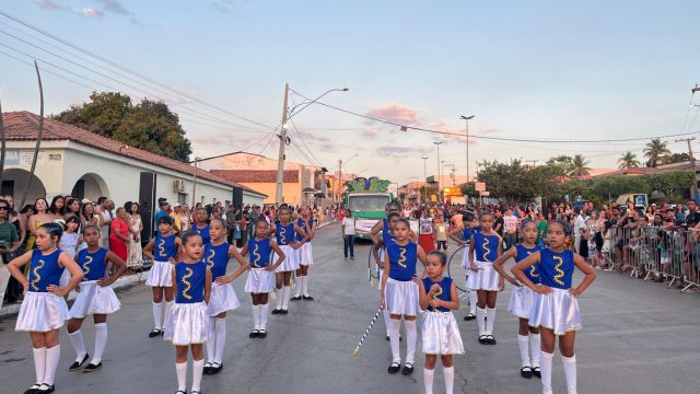 Crianças com uniformes azuis e saias brancas, algumas segurando bastões, participam do Desfile de 7 de Setembro em Correntina. O público acompanha a apresentação nas laterais da rua.