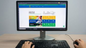 Pessoa utiliza um computador de mesa para acessar o portal oficial da Prefeitura de Correntina. Na tela, a página inicial apresenta o destaque