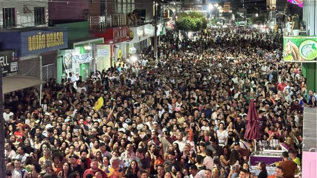 Multidão ocupa avenida comercial durante evento noturno em Correntina, com centenas de pessoas reunidas em frente a lojas e prédios iluminados, formando um grande público concentrado ao longo da rua.