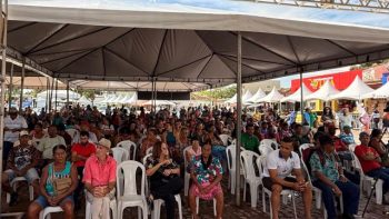 Moradores reunidos sob tendas na Praça do Mercado Velho durante a distribuição de alimentos da Semana Santa, sentados em cadeiras e aguardando atendimento, com grande participação da comunidade.