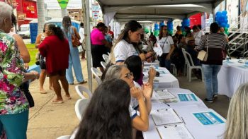 Pessoas sendo atendidas em uma ação de saúde ao ar livre, com profissionais organizados em mesas sob tendas, realizando cadastro e orientações à população em um espaço público de Correntina.