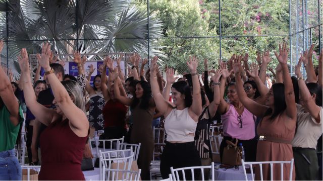 Professores e profissionais da rede municipal participam da Jornada Pedagógica 2026, reunidos em espaço coberto, com as mãos erguidas durante dinâmica de integração.