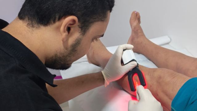 Profissional com luvas utiliza aparelho sobre a perna de uma paciente durante atendimento do Cuidar Correntina.