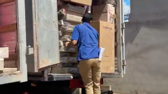 Homem descarrega caixas de móveis e eletrodomésticos de um caminhão, durante ação de entrega para famílias beneficiadas.
