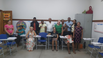 Grupo de alunos da Educação de Jovens, Adultos e Idosos (EJAI) posando para foto em sala de aula em Correntina. Alguns estão sentados em carteiras escolares azuis com cadernos e apostilas, enquanto outros estão em pé ao fundo, sorrindo. O ambiente é acolhedor, com cartazes coloridos nas paredes e frases de incentivo à educação. A diversidade de idades e perfis evidencia o compromisso do município com a inclusão educacional.
